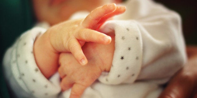 Closeup of small hands of a newborn baby separating the little fingers.Baby is held in the mother's arms.