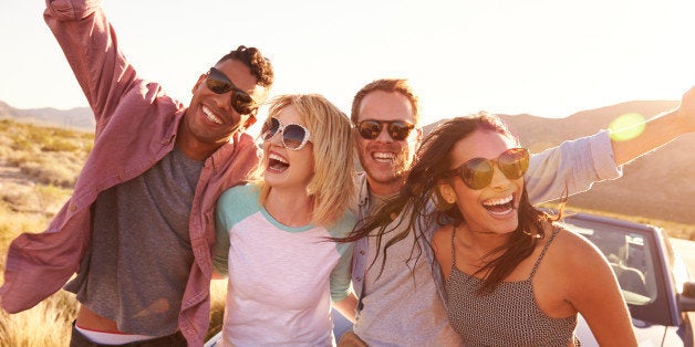 Friends On Road Trip Sitting On Hood Of Convertible Car