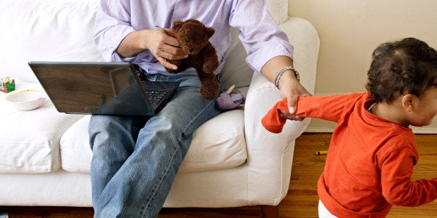 father working with laptop computer at home while little son is playing