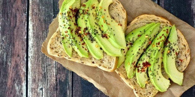 Open avocado sandwiches with whole grain bread on paper against a rustic wooden background