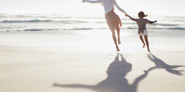 Mother and daughter holding hands and running on sunny beach