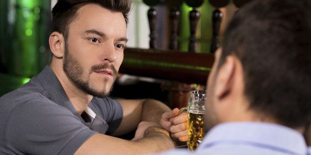 Two young men talking to each while drinking beer in bar
