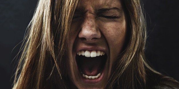 A young woman screaming uncontrollably while isolated on a black background