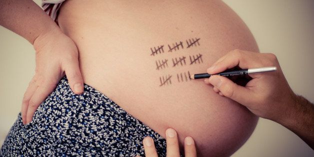 Heavily pregnant lady with 39 tally marks / hash marks counting 39 weeks of pregnancy. A man's hand is drawing the counting lines with a black pen.