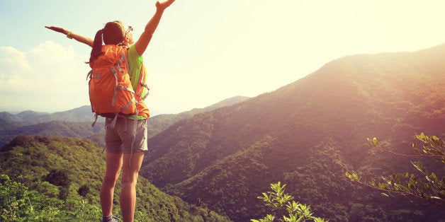 cheering woman hiker open arms at mountain peak cliff