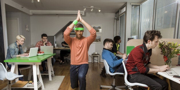 Young man exercising while colleagues work