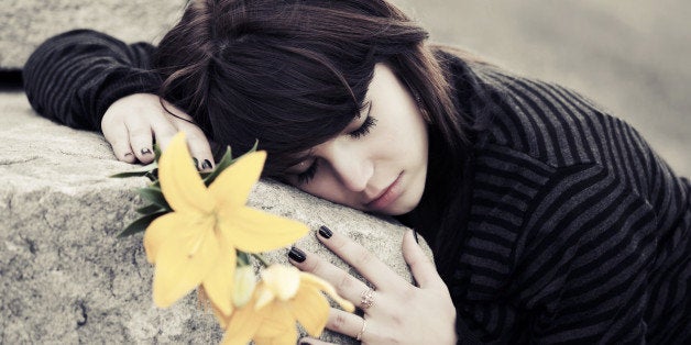 Sad young woman with a flowers lying on tombstone