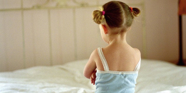 Girl (2-4) sitting on bed, rear view