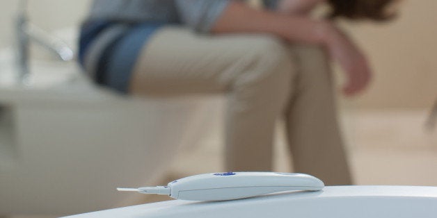 Unhappy woman in bathroom with pregnancy test