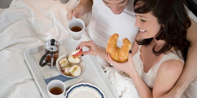 Portrait of happy young couple relaxing and having breakfast in bed
