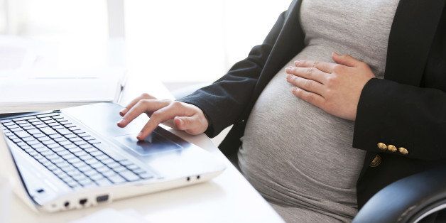 Cropped image of pregnant businesswoman typing something on laptop while sitting at her working place in office