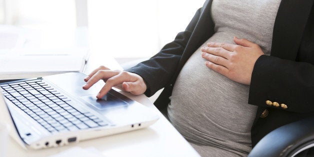 Cropped image of pregnant businesswoman typing something on laptop while sitting at her working place in office