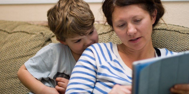 Mother and son sitting on a living room couch sharing an intimate moment while she teaches him on a tablet computer. It is amazing how a mother can interact with a child. He is so captivated not by the tablet but by his mom teaching him.