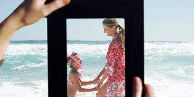 Female hands framing mother and daughter playing in water at beach