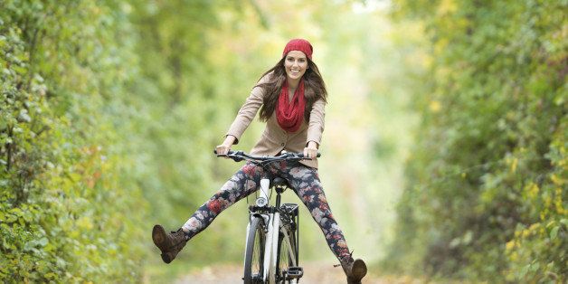 Beautiful woman with a perfect natural expression riding her bicycle through an autumn forest. Nikon D800e. 