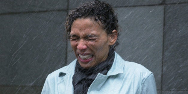 Mature woman standing in rain holding microphone, eyes tightly closed