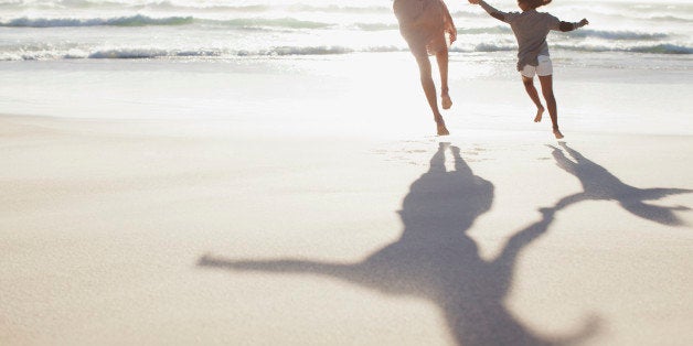 Mother and daughter holding hands and running on sunny beach