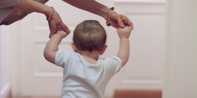 young mother helping her baby boy in his first steps at home