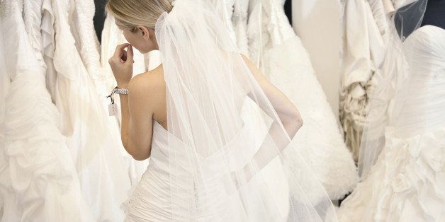 Back view of a young woman in wedding dress looking at bridal gowns on display in boutique