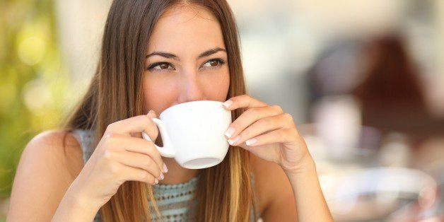 Woman drinking a coffee from a cup in a restaurant terrace while thinking and looking sideways