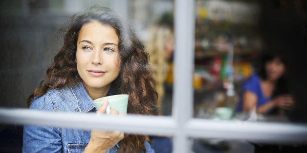Lifestyle image of woman looking out of a cafe window whilst holding a drink.