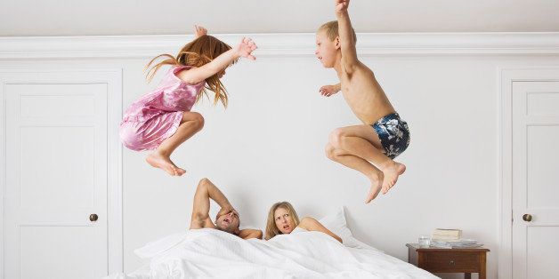 Family of four on bed, children (6-8) jumping, side view