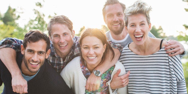 Group portrait of happy friends enjoying picnic at lakeshore