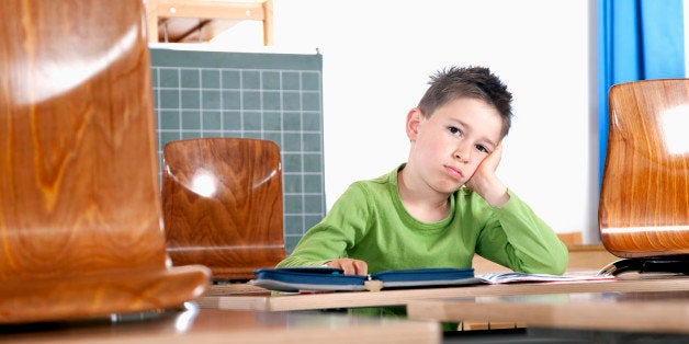 portrait of young boy sitting alone in classroom