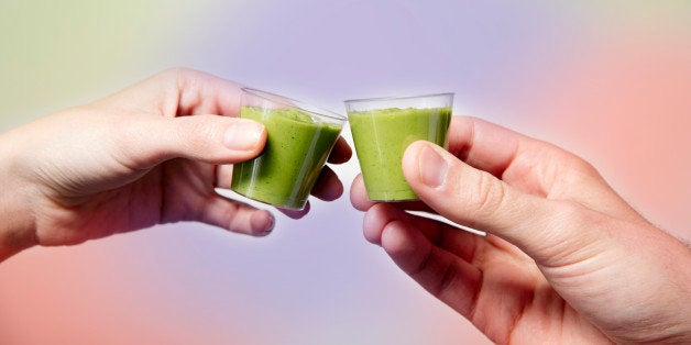 Close up of young woman and man's hands toasting with green smoothie shots