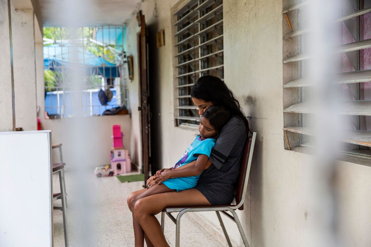 Betsy Rosado Sánchez comforts her youngest daughter, 6-year-old Marina, on their front porch. Marina, like her older sister Yermiletsy, had to change schools.