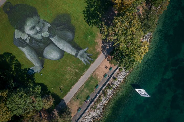 This aerial view shows French artist Saype's giant land art fresco representing a little girl droping an origami boat into Lake Geneva.