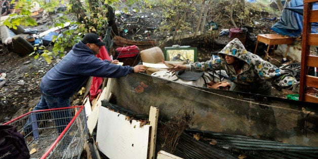 Carlos Tovar, a contractor in charge of cleanup, left, hands out a warning notice to a resident of the Silicon Valley homeless encampment known as The Jungle, Monday, Dec. 1, 2014, in San Jose, Calif. City officials began posting notices on hand built structures, tents and tree trunks warning the 200 residents of what is likely the nation's largest homeless encampment that the bulldozers are coming. People living in the Silicon Valley camp must be out by Thursday, Dec. 4 or face arrest for trespassing. (AP Photo/Marcio Jose Sanchez)