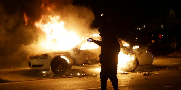 A man runs from a police car that is set on fire after a group of protesters vandalize the vehicle after the announcement of the grand jury decision Monday, Nov. 24, 2014, in Ferguson, Mo. A grand jury has decided not to indict Ferguson police officer Darren Wilson in the death of Michael Brown, the unarmed, black 18-year-old whose fatal shooting sparked sometimes violent protests. (AP Photo/Charlie Riedel)