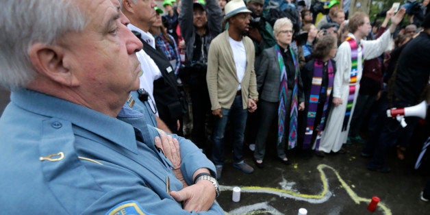 A Ferguson, Mo., police officer stands in the driveway at the police station near a chalk drawing made as a memorial to Michael Brown, Monday, Oct. 13, 2014, in Ferguson. Activists planned a day of civil disobedience to protest the shooting Michael Brown and a second police shooting in St. Louis. (AP Photo/Charles Rex Arbogast)