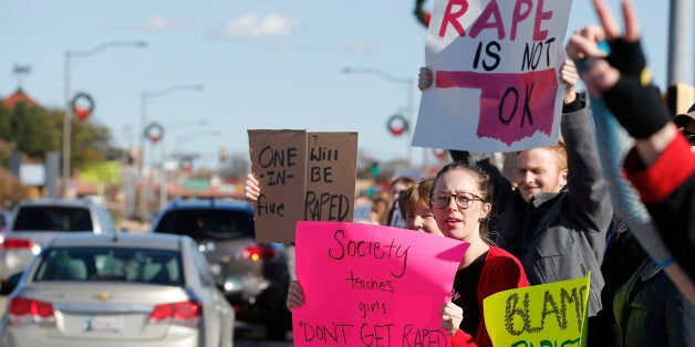FILE - In this Nov. 24, 2014, file photo, Norman resident and University of Oklahoma law school student Carly Haiduk, left, and Cole Singleton, a junior at Norman North High School, hold signs during protest across the street from Norman High School in Norman, Okla. Police say they have arrested Tristen Kole Killman-Hardin, 18, a former Norman High School student, and accused him of raping an unconscious girl, alleging heᅢ까タᅡルs responsible for an attack that helped trigger protests by his former classmates. (AP Photo/Sue Ogrocki, File)
