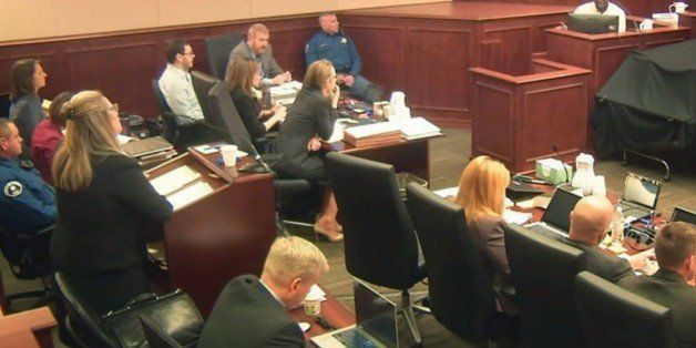 FILE - In this April 27, 2015 file image taken from Colorado Judicial Department video, Colorado theater shooter James Holmes, left rear in light-colored shirt, watches during testimony by witness Derick Spruel, upper right, on the second day of his trial in Centennial, Colo. During the first two weeks of Holmes' trial so far, jurors have asked more than 100 questions of witnesses, through notes passed to the judge. While absorbing much testimony describing the mayhem in the movie theater on the night of the killings, jurors are also grappling with the central question of the case: Was Holmes legally insane when he began shooting? (Colorado Judicial Department via AP, Pool, File)