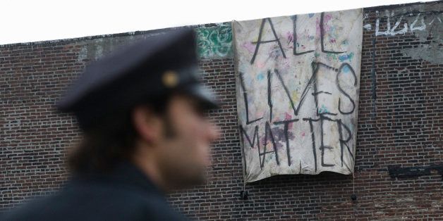 A sign that reads "ALL LIVES MATTER" is hung from a building near a makeshift memorial at the site where NYPD officers Rafael Ramos and Wenjian Liu were murdered in the Brooklyn borough of New York, Monday, Dec. 22, 2014. Police say Ismaaiyl Brinsley ambushed the two officers in their patrol car in broad daylight Saturday, fatally shooting them before killing himself inside a subway station. (AP Photo/John Minchillo)