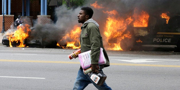 A man carries items from a store as police vehicles burn, Monday, April 27, 2015, after the funeral of Freddie Gray in Baltimore. Gray died from spinal injuries about a week after he was arrested and transported in a Baltimore Police Department van. (AP Photo/Patrick Semansky)