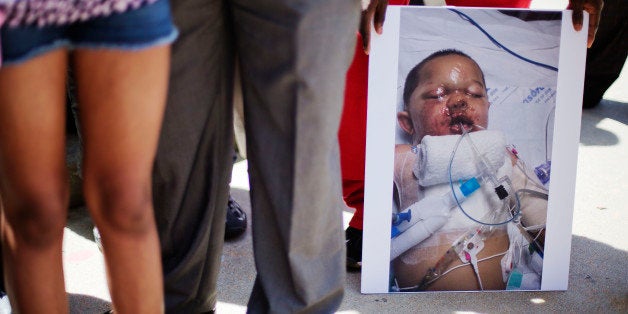 A photo of 19-month-old Bounkham Phonesavanh who was severely burned by a flash grenade during a SWAT drug raid, is held by a supporter during a vigil outside Grady Memorial Hospital where he is undergoing treatment, Monday, June 2, 2014, in Atlanta. A Georgia state senator says he will ask U.S. Attorney Sally Quillian Yates to investigate a police raid where the Georgia toddler was severely burned by a flash grenade. State Sen. Vincent Fort joined 19-month-old Bounkham Phonesavanh's family at a prayer vigil outside Grady Memorial Hospital in Atlanta on Monday. The boy's mother says a fever may delay a planned surgery. Police have said officers were looking for a suspect who may have been armed and didn't know children were inside. (AP Photo/David Goldman)