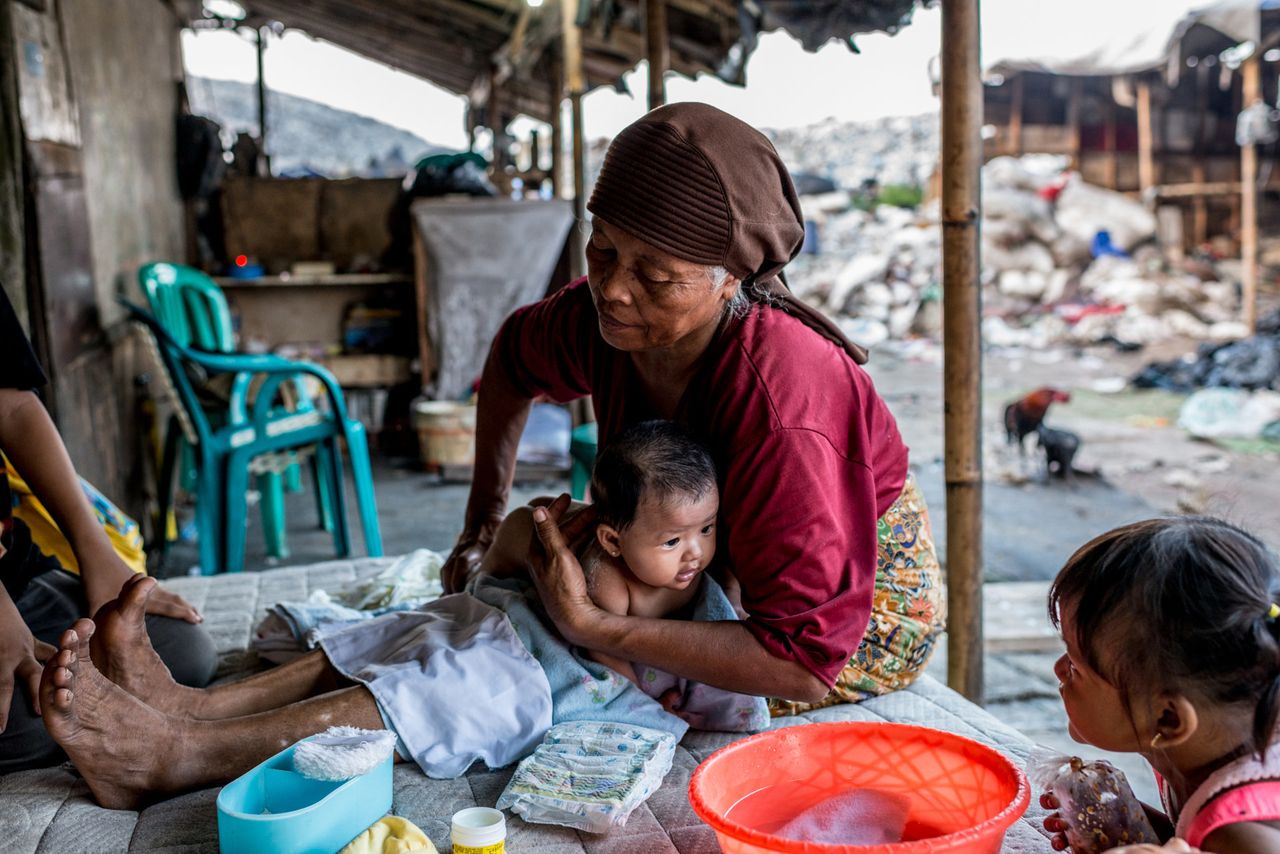 Mak Muji washes Reza's sister, Aysila Husna, 3 months old. Mak Muji did not deliver the newborn because the family had enough money for a hospital birth this time. But they still live in their shack at the landfill, and Mak Muji visits often.