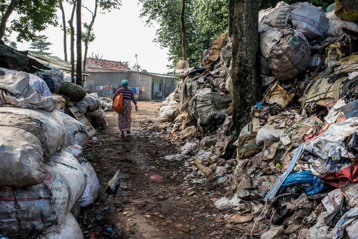 Mak Muji walks through heaps of waste on her way to one of the landfill villages. The orange bag slung over her shoulder holds the scale she uses to weigh newborn babies. 