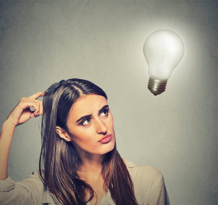 Closeup portrait beautiful girl woman thinks looking up at bright light bulb isolated on gray wall background. Idea, business, education and people concept. Human face expression