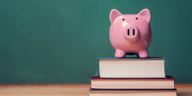 Pink Piggy bank on top of books with chalkboard in the background as concept image of the costs of education