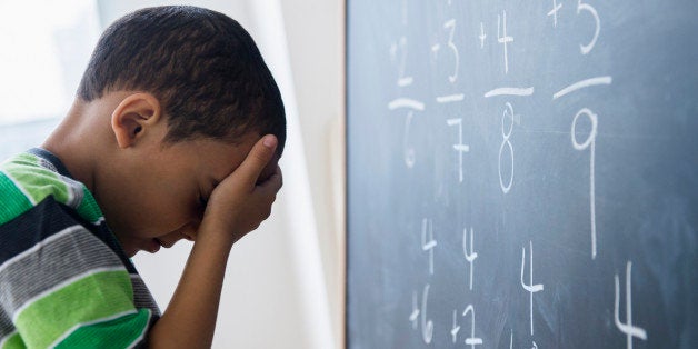 Mixed race boy doing math problems at board in class