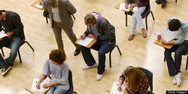 Professor walking by college students taking test in classroom