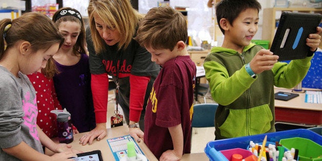 Andrew Zhu, right, smiles while using his iPad for a lesson as first grade teacher Jan Sabin helps Hayden Putz, left, with he