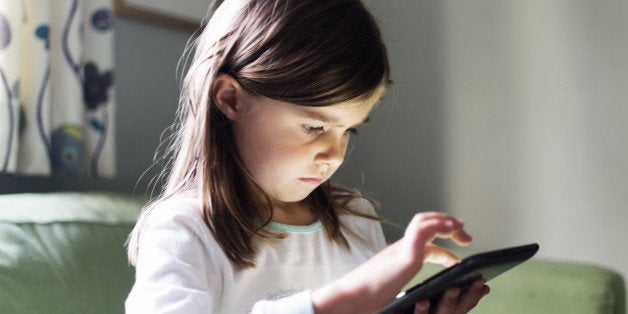 A young girl uses a tablet computer late at night with the glow from the screen on her face.