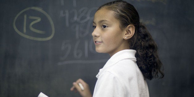 Ten year old Hispanic girl solves math problem in classroom.