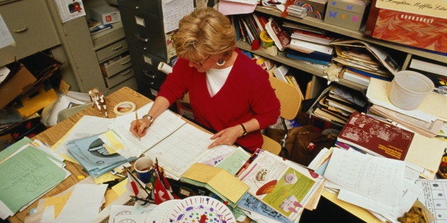 Primary school teacher working at crowded desk in cramped office