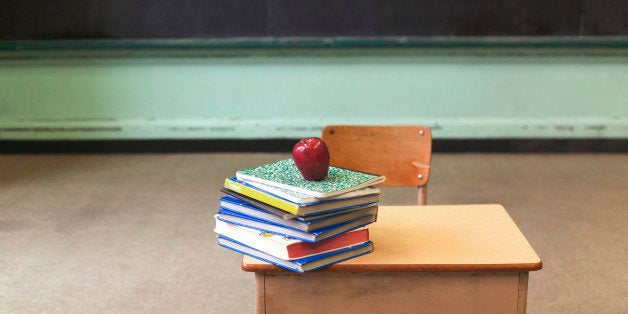 Stack of school books and apple on desk in empty classroom